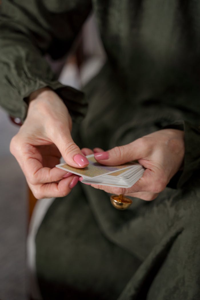 A close-up of a woman shuffling playing cards indoors, dressed in green.